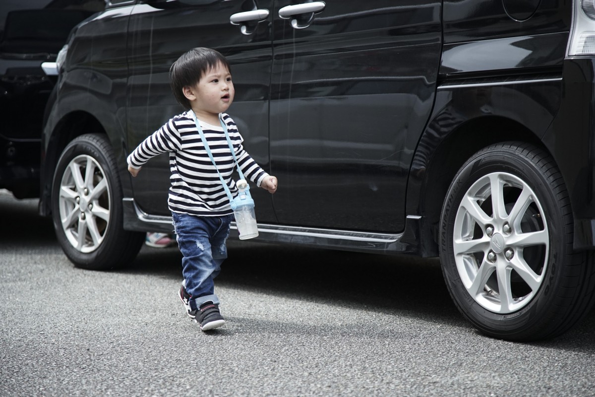 A young boy standing in front of a car